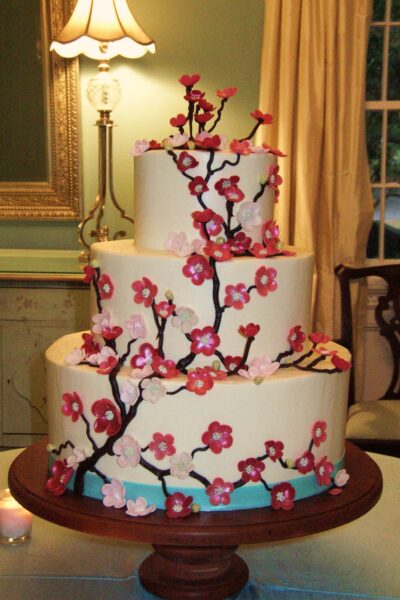Elegant white tiered cake decorated with pink cherry blossoms and branches.