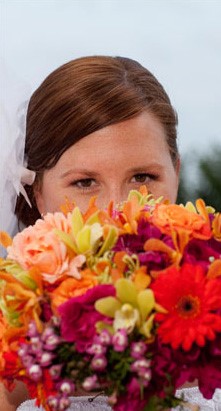 Bride peeking over a vibrant bouquet of flowers.