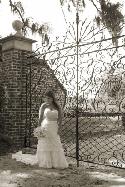 Bride standing by ornate wrought iron gate.
