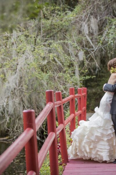 Bride and groom embracing on red bridge.