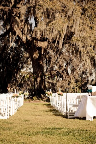 Outdoor wedding setup with white chairs, tables.