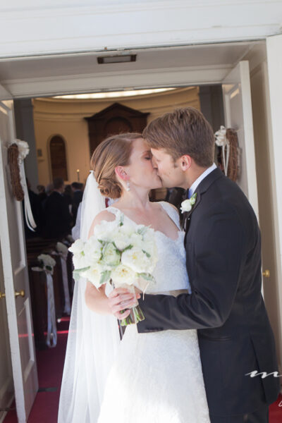 Bride and groom kissing at church entrance.