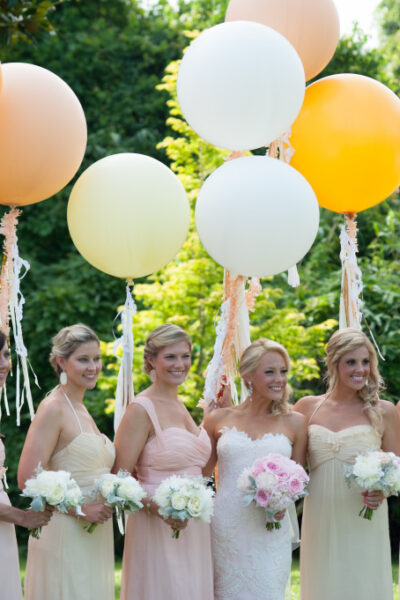 Bridesmaids with balloons and bouquets outdoors.