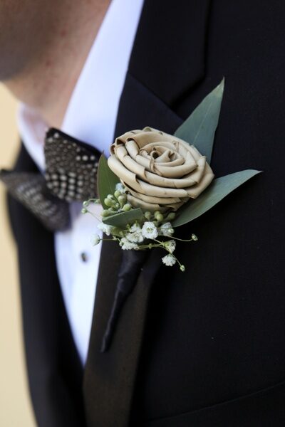 Elegant boutonniere with a beige rose on a black tuxedo lapel.