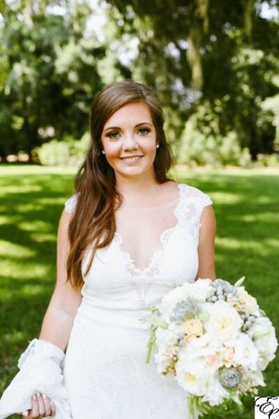 Bride in a white wedding dress holding a bouquet outdoors.