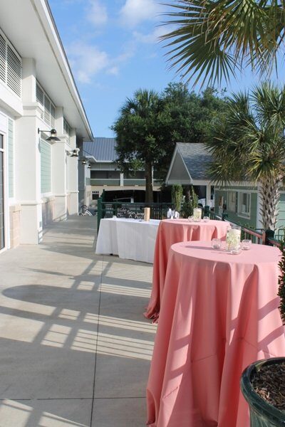 Outdoor event setup with pink tablecloths and greenery in the background.