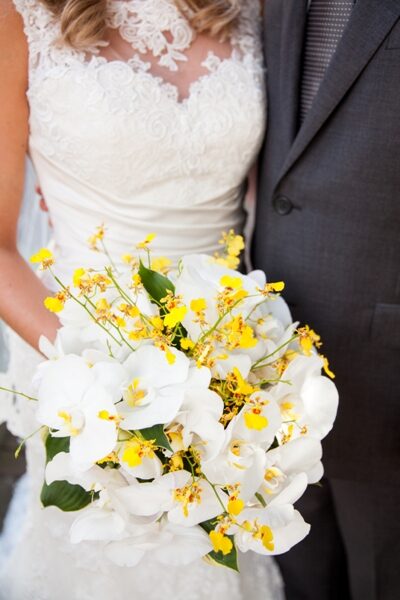 Bride and groom holding a bouquet of white and yellow flowers.