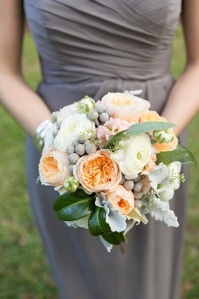 A bouquet of peach and white flowers held by a person in a gray dress.