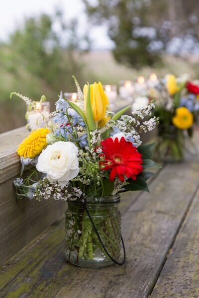 A vibrant bouquet with yellow, red, and white flowers in a glass vase outdoors.