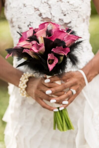 Hands holding a bouquet of pink calla lilies and white flowers.