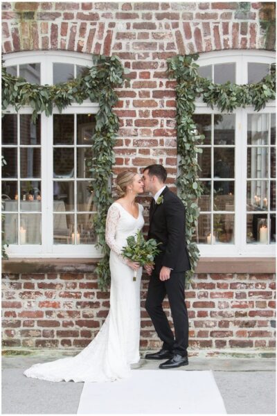 Bride and groom kissing, brick backdrop.