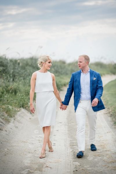 A couple holding hands and walking outdoors in elegant attire.