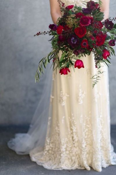 A bridal bouquet featuring deep red flowers and greenery.