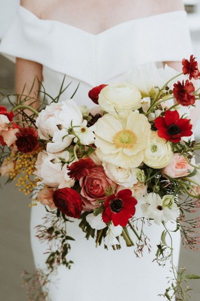 Elegant bouquet of white and red flowers held by a person in white.