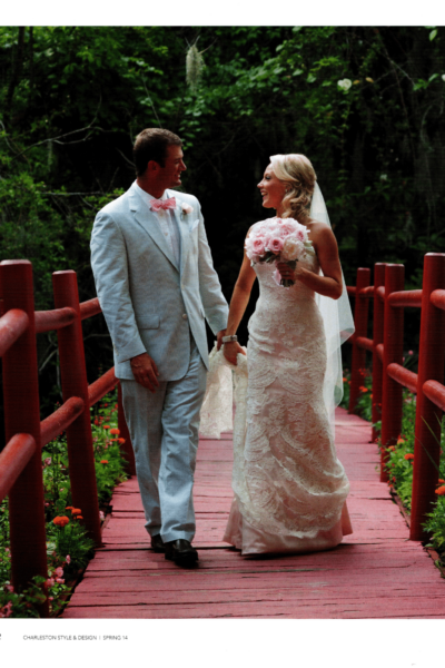 Bride and groom walking hand-in-hand on a red wooden bridge outdoors.