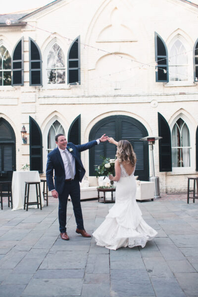 Bride and groom dancing joyfully outdoors by a historic building.