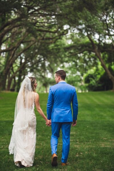Bride and groom walking hand in hand in a green park.