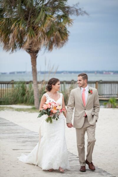 Bride and groom walking outdoors near the beach, smiling at each other.