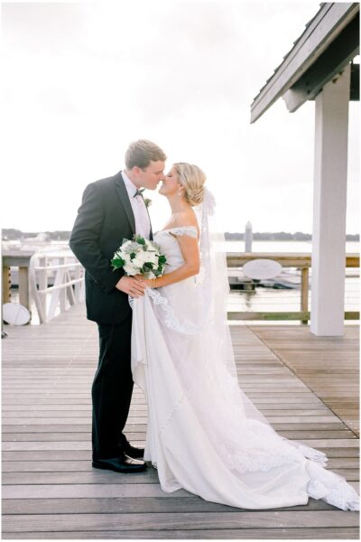 Bride and groom sharing a kiss on a dock by the water.