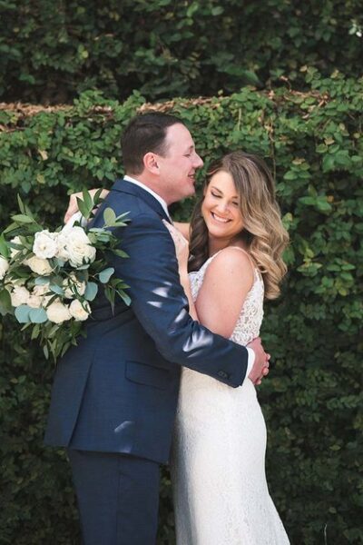 Bride and groom embracing outdoors with a bouquet.