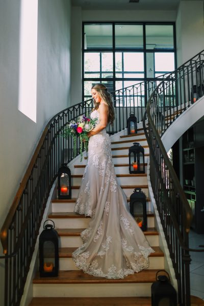 Bride in elegant gown holding flowers on a staircase.
