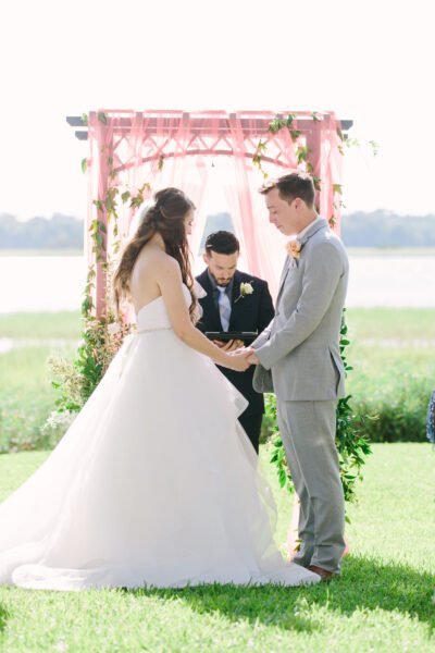 Couple exchanging vows during an outdoor wedding ceremony by a lake.