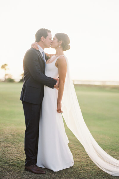 Bride and groom sharing a romantic kiss outdoors at sunset.