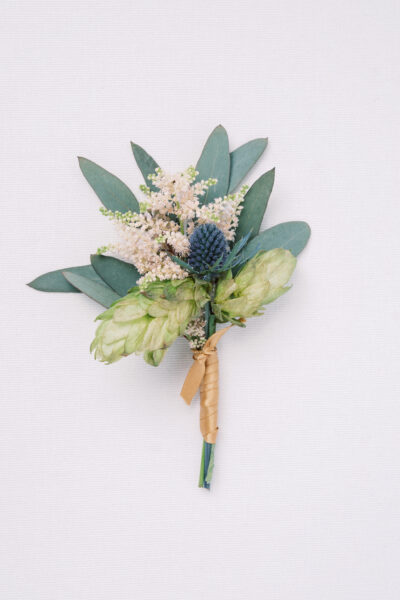 Elegant boutonniere with green hops, white flowers, and dark berries.