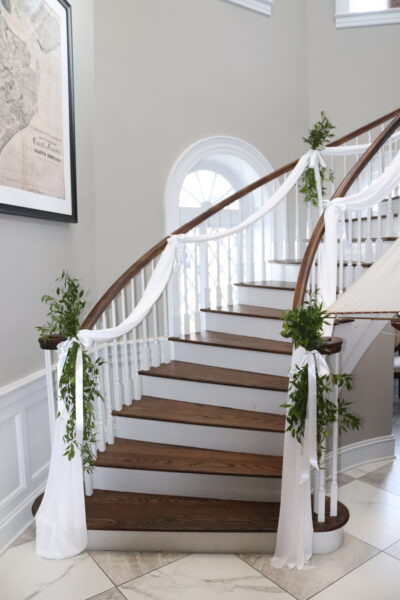 Elegant staircase decorated with white drapes and greenery for a special event.