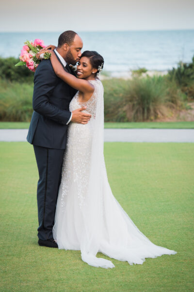 Bride and groom embracing outdoors by the water.