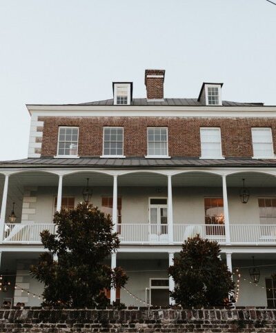 Large historic brick house with wrap-around porch and chimneys.