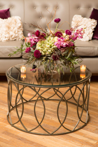 Elegant glass coffee table with floral centerpiece and candles in cozy living room.
