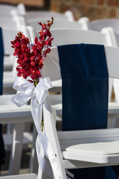 Chair decorated with navy blue cloth and white bow with red flowers.