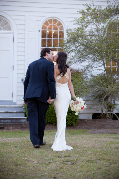 Bride and groom share a kiss outside a white building after their wedding.