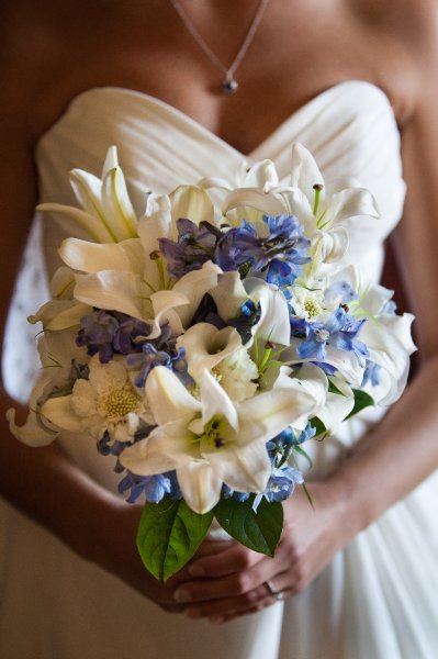 Bride holding a bouquet with white lilies and blue flowers.