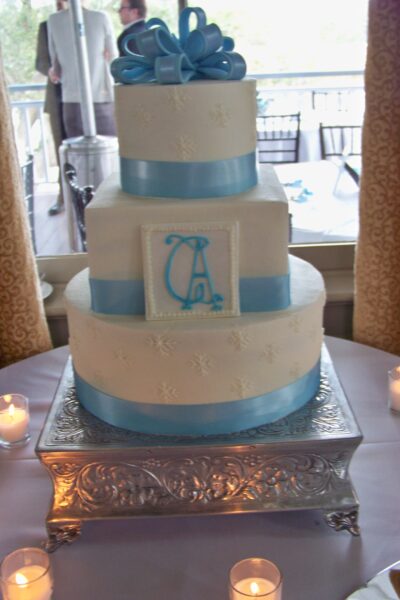 Three-tiered white cake with blue ribbons and a monogram on the middle tier.