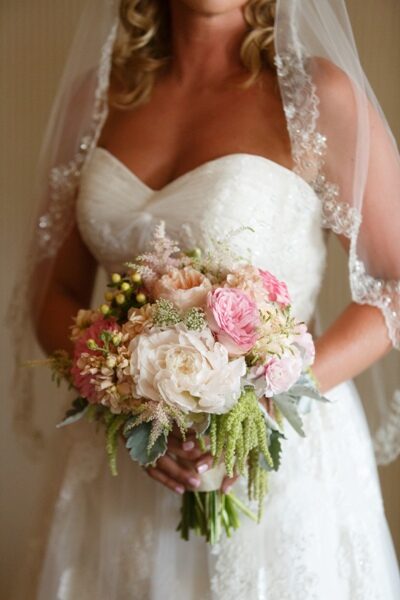 Bride holding a delicate bouquet of roses and greenery.