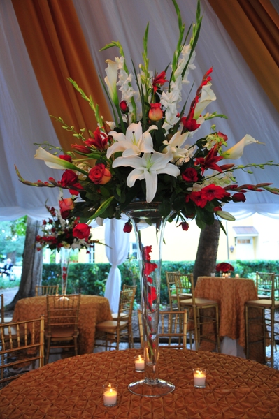 Elegant floral centerpiece with white lilies and red flowers on a tall glass vase.