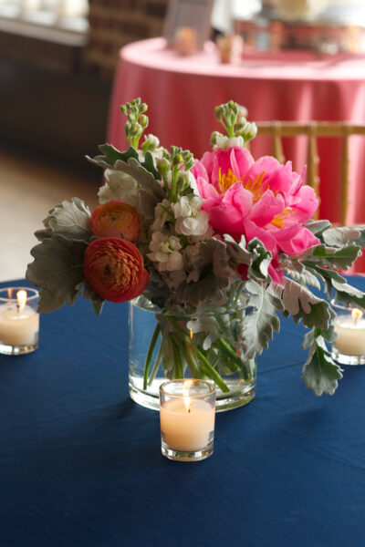 A vibrant pink flower arrangement in a glass vase on a navy tablecloth.