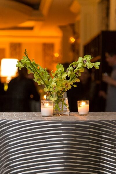 A floral centerpiece with candles on a striped tablecloth in warm lighting.