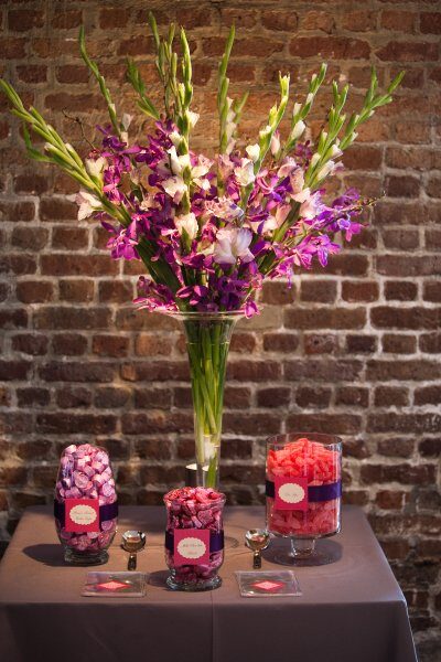 Vibrant purple and pink flowers arranged in a tall glass vase with matching floral decorations below.