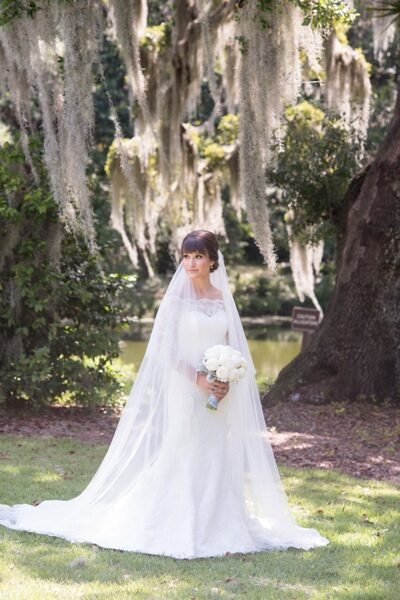 Bride in white wedding gown standing outdoors with hanging moss.