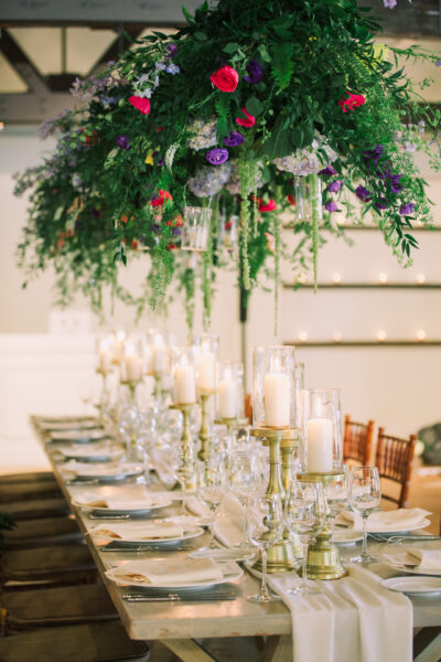 Elegant dining table with candles and floral centerpiece under hanging greenery.