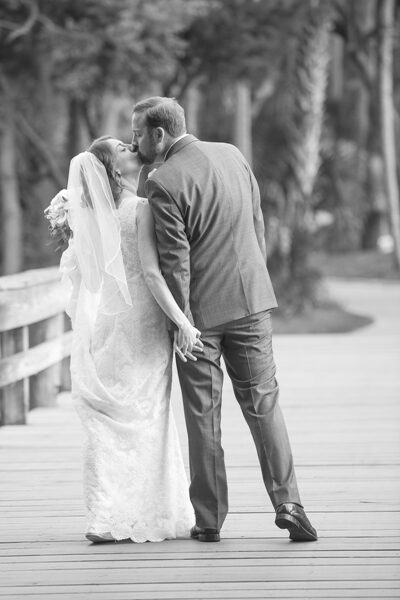 Black and white photo of a bride and groom holding hands on a wooden bridge.