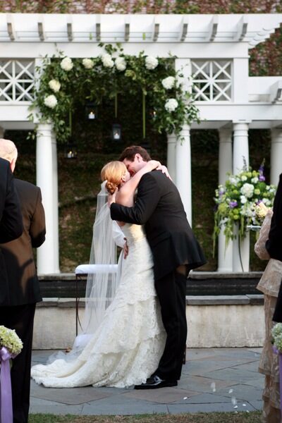 Bride and groom share a kiss during their outdoor wedding ceremony.