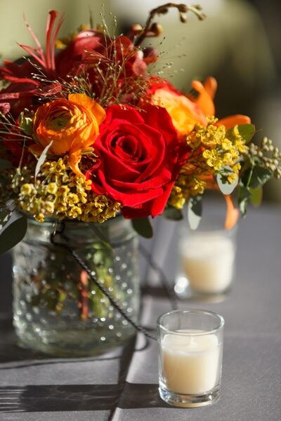 A vibrant red rose in a mixed floral arrangement with soft candlelight.