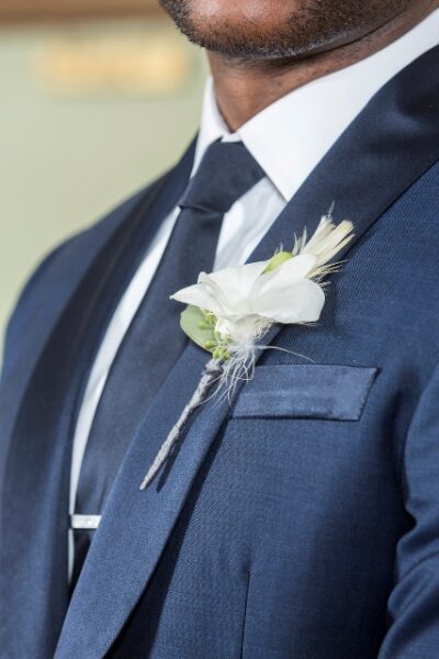 Close-up of a groom's navy suit with a white boutonniere and tie clip.