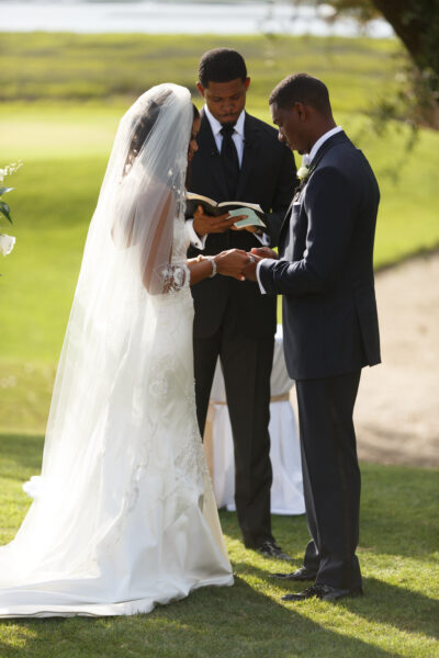A bride and groom exchanging rings during an outdoor wedding ceremony.
