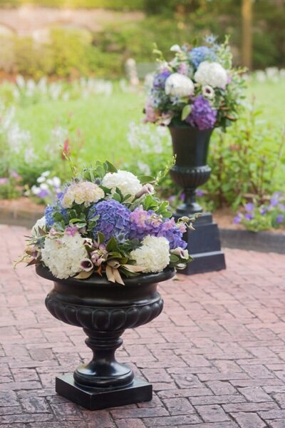 Elegant floral arrangements in black urns on a brick path.