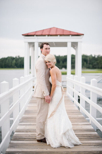 Bride and groom holding hands on a dock over a lake.